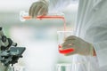 Closeup shot of orange red reagent in glass volumetric cylinder poured in beaker by scientist in white lab coat and rubber gloves