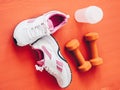 Closeup shot of pair of sports shoes, dumbbells and water tumbler isolated on orange surface