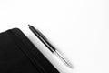 Closeup shot of a pen near a black notebook on a white surface Royalty Free Stock Photo
