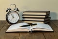 Closeup shot of a pen on a notebook, books, and an alarm clock on a desk