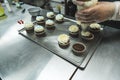 Closeup shot of person adding vanilla buttercream frosting with pastry bag onto chocolate muffins placed on stainless