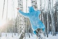 Closeup shot of a person in a fluffy blue costume climbing a bare birch tree in a forest in winter Royalty Free Stock Photo