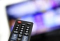 Closeup shot of a person holding a black remote control in front of the TV Royalty Free Stock Photo