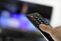 Closeup shot of a person holding a black remote control in front of the TV Royalty Free Stock Photo