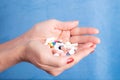 Closeup shot of a person holding a handful of different pills with a blue background