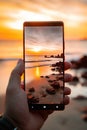 closeup shot of person holding mobile phone in hand and taking photo of sunset at sea, nature photography with Royalty Free Stock Photo