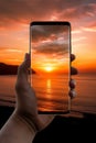 closeup shot of person holding mobile phone in hand and taking photo of sunset at sea, nature photography with Royalty Free Stock Photo