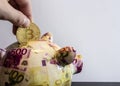 Closeup shot of a person tossing a coin into a piggy bank