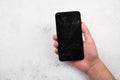 Closeup shot of a person& x27;s hand holding a cracked smartphone against a rusty wall background