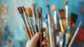 A closeup shot of a persons hand holding various paintbrushes trying to decide which one will be best for their DIY