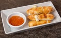 Closeup shot of a pile of delicious cheese rolls and orange sauce on a white plate