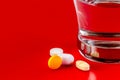 Closeup shot of pills with a glass of water on the side on a red background Royalty Free Stock Photo