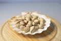 Closeup shot of pistachios in a seashell-shaped vase on a round wooden plate Royalty Free Stock Photo