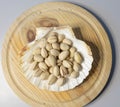 Closeup shot of pistachios in a seashell-shaped vase on a round wooden plate Royalty Free Stock Photo