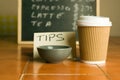 Closeup shot of plastic coffee cup and bowl for tips with a pricelist background