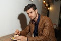 Closeup shot of a pretty male in brown leather jacket holding coffee spoon and stirring hot coffee