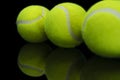 Closeup shot of the reflection of three tennis ball on a reflective black surface