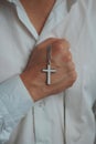 Closeup shot of a religious male holding a silver necklace with a cross pendant