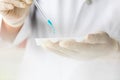 Closeup shot of scientist wears white lab coat and rubber gloves hands holding orange red reagent in glass dropper dropping into