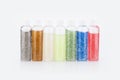 Closeup shot of seven bottles of colorful glitter on a white background