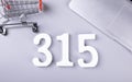 Closeup shot of small shopping cart, a laptop, and the number 315-concept of financial freedom Royalty Free Stock Photo