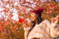 Closeup shot of a smiling Southeast Asian girl holding a red smartphone and wearing a warm hat