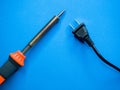 Closeup shot of a soldering iron and a black American plug on a blue surface