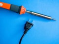 Closeup shot of a soldering iron and a black American plug on a blue surface