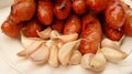 Closeup shot of a stack of cooked meat sausages and a lot of garlic cloves on a plate