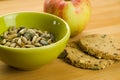 Closeup shot of sunflower and pumpkin seeds in a bowl, apple, and oatcakes