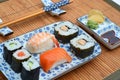 Closeup shot of sushi rolls, sauce, and dumplings in plates next to chopsticks on bamboo table cover Royalty Free Stock Photo