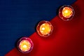 Closeup shot of three flower-shaped burning candles in a diagonal row on a red and blue surface Royalty Free Stock Photo