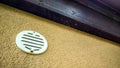 Closeup shot of a ventilation cap on a yellow painted wall with  dark wooden plank on top Royalty Free Stock Photo