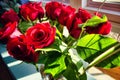 Closeup shot of vibrant bright red roses with leaves in a vase