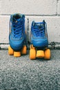 Closeup shot of vintage blue quad roller skates with orange wheels against white wall