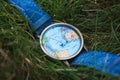 Closeup shot of a watch with a design of the world map on the grassy terrain