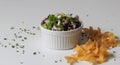 Closeup shot of a white bowl of a vegetable salad with raw pasta on the side on a white surface