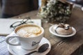 Closeup shot of a white ceramic coffee cup with latte art coffee near doughnut in a plate on table