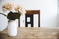 Closeup shot of white flowers in a white jar on a wooden table with a blurred background Royalty Free Stock Photo