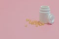 Closeup shot of a white pill container and yellow capsules on a pink background Royalty Free Stock Photo