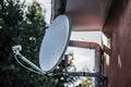 Closeup shot of a white satellite dish on fixed on a brown wall with trees on the background Royalty Free Stock Photo