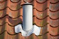 Closeup shot of a white steel chimney on an old brown tile roof outside. Stay warm this winter with a fireplace. Light a