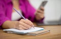 Closeup shot of woman holding smartphone and writing in notepad Royalty Free Stock Photo