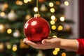 shot of a woman\'s hand placing a red Christmas ball on the Christmas tree