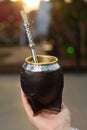 Closeup shot of the woman's hand holding a black mate cup with mate bombilla.