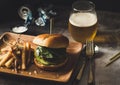 Closeup shot of a wooden plate with a burger and french fries, beer cans in the background Royalty Free Stock Photo