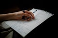 Closeup shot of a writer writing a poem in a notebook with a dark background