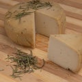 Closeup shot of yellow caciotta cheese with herbs on a striped wooden cutting board