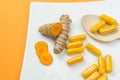 Closeup shot of yellow Curcuma root and pills with a wooden spoon on orange background Royalty Free Stock Photo