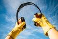 Closeup shot of yellow gloved hands holding red noise canceling construction headphones to blue sky